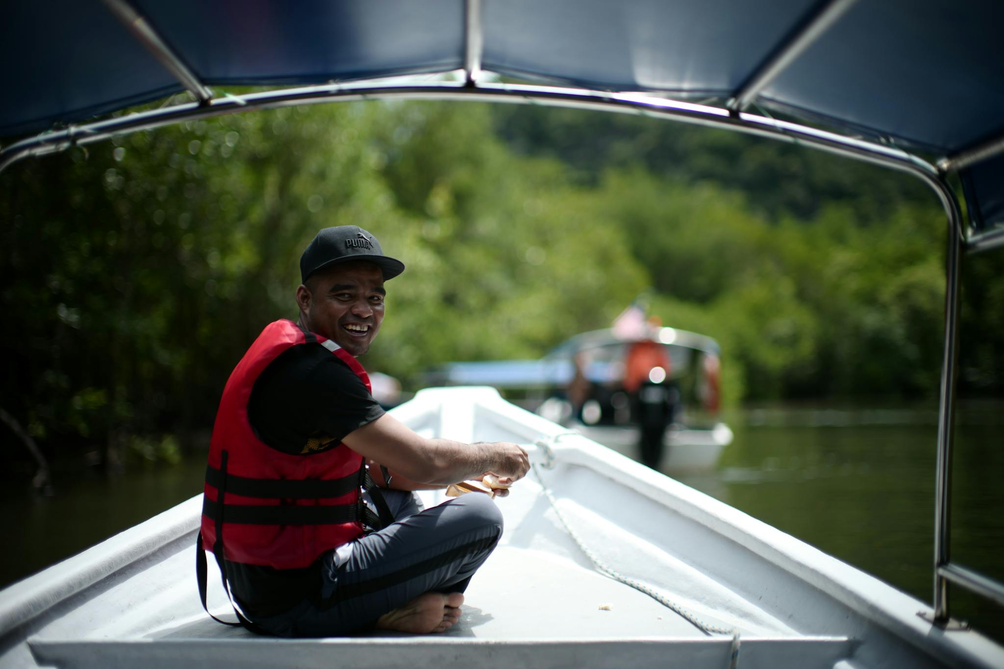 A smiling man in a red life jacket enjoys a boat ride on a lush green river in Langkawi, Malaysia.